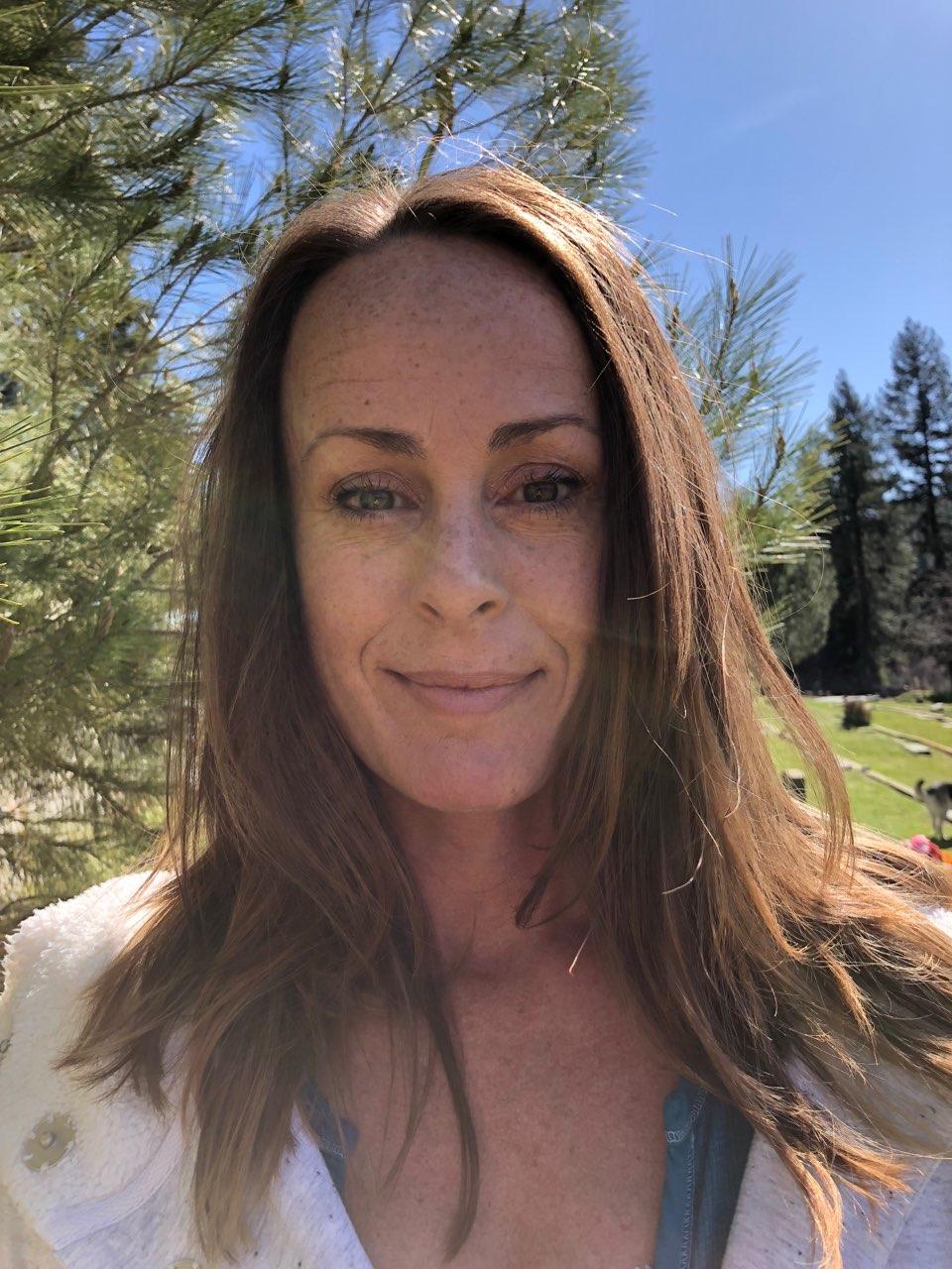 Portrait of Kristen Michelle Nale outdoors, framed by sunlit pine branches