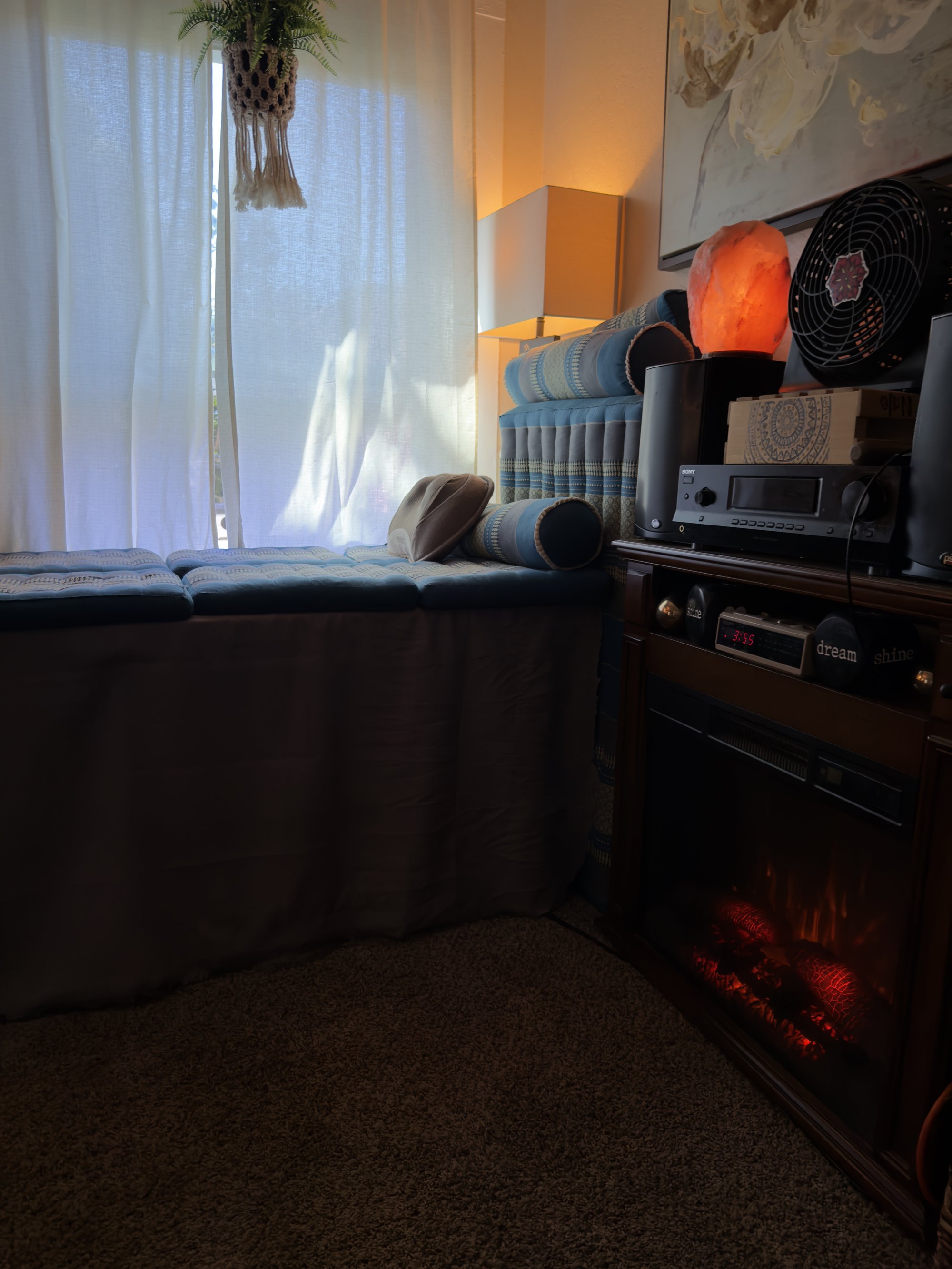 Side cabinet with stereo equipment, a fan, a glowing Himalayan salt lamp, and the warm red light of an electric hearth below.