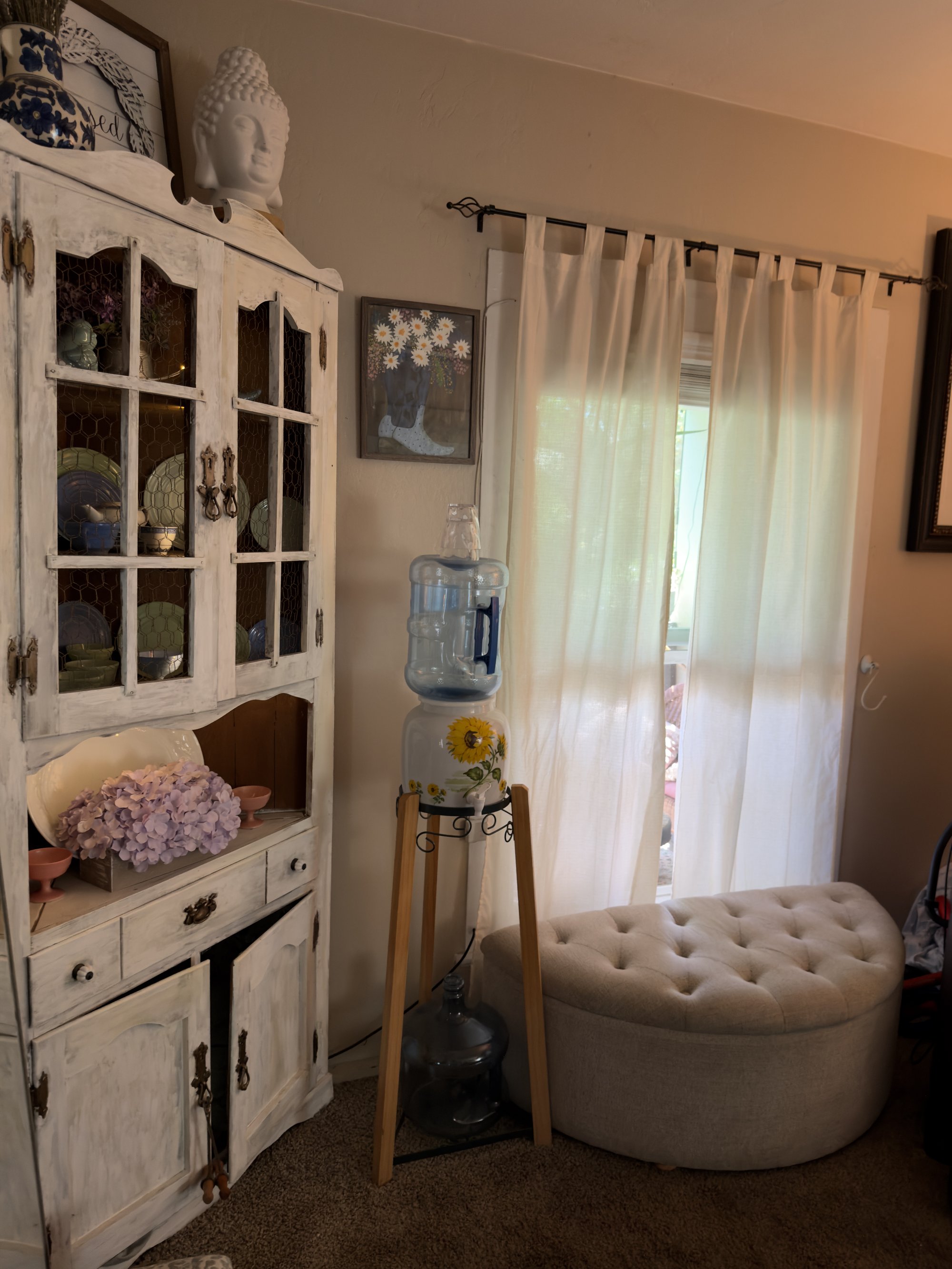 A white window-style cabinet with mirrored panes, holding small ceramic decorations — green pots, a ceramic flower bouquet in lilac and blue.