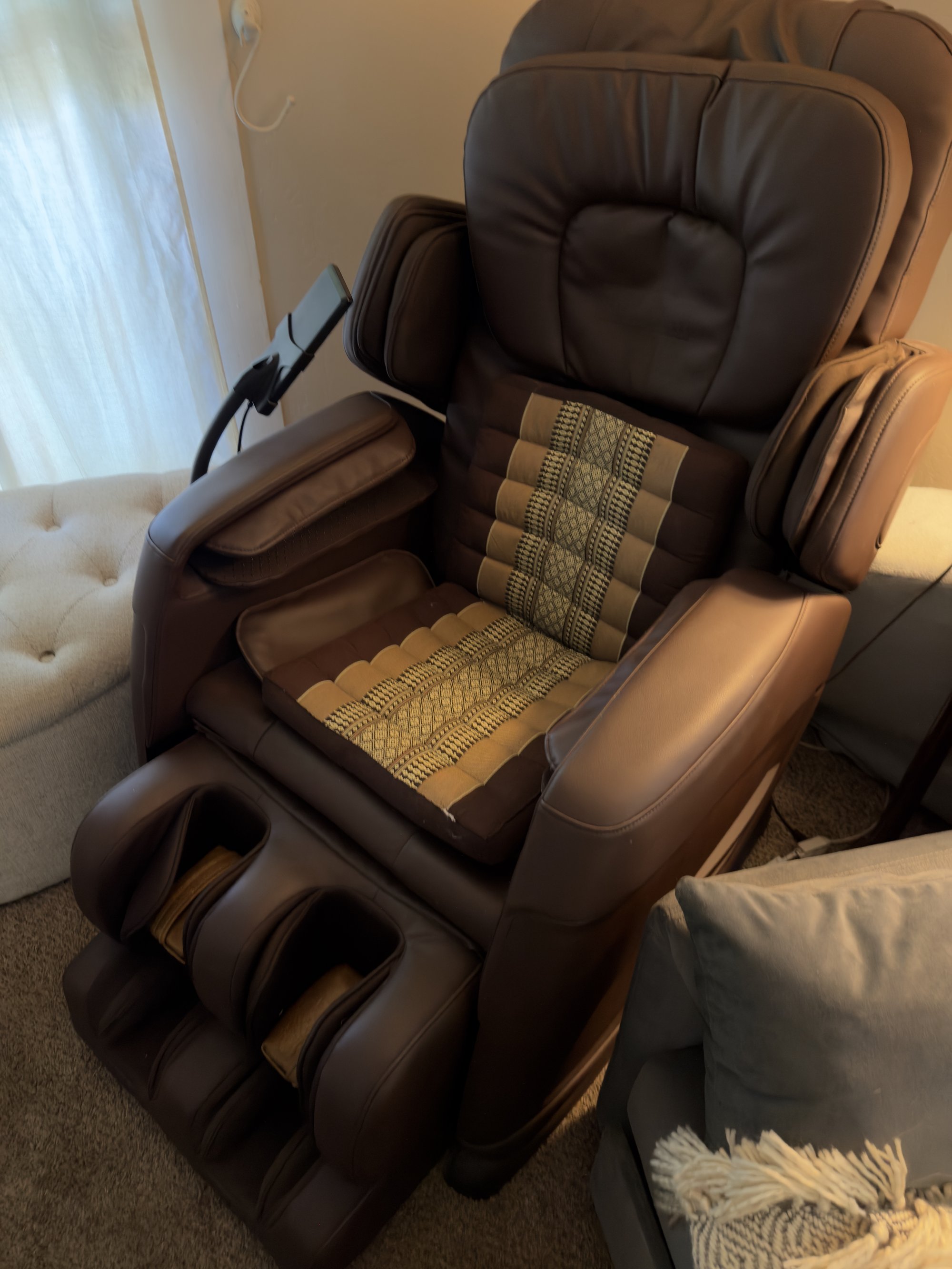 Close-up of the massage chair — brown leather, Thai striped cushion across the seat, gentle daylight from the window behind.