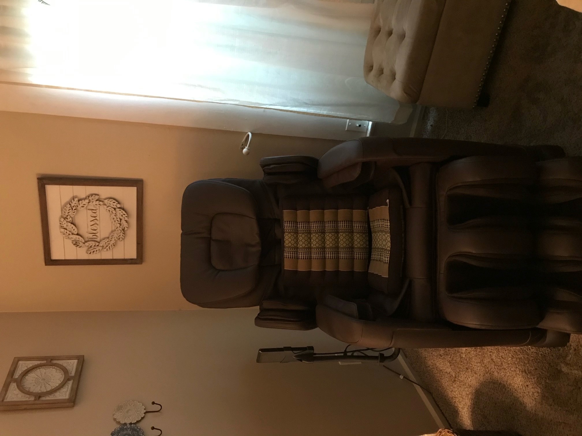 High-end brown leather reclining massage chair with a tan striped cushion, "Blessed" wreath on the wall behind.