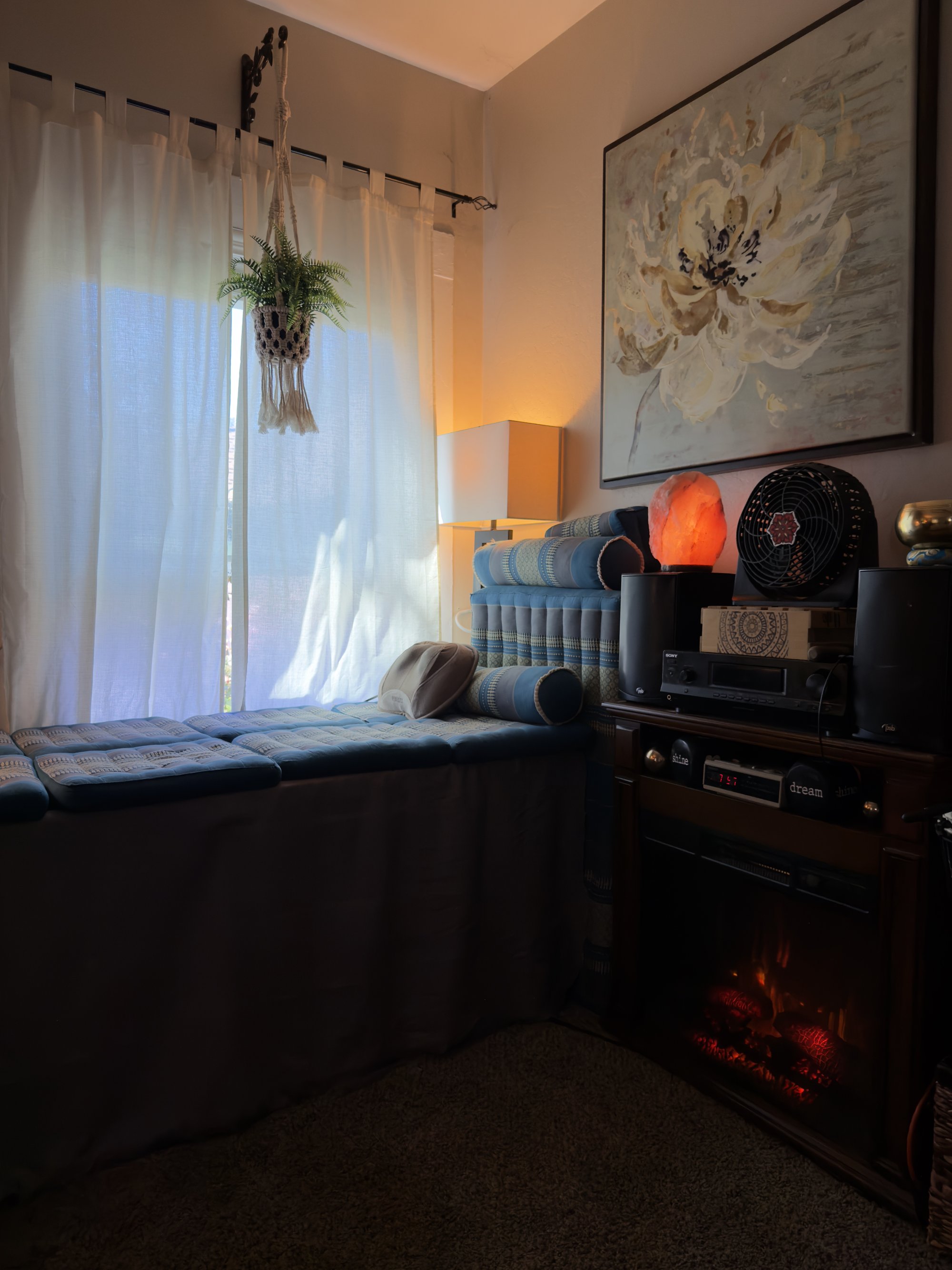 Room view with a large white-flower painting on the wall, salt-lamp glow, dried lavender in a vase, a heater's warm light below.