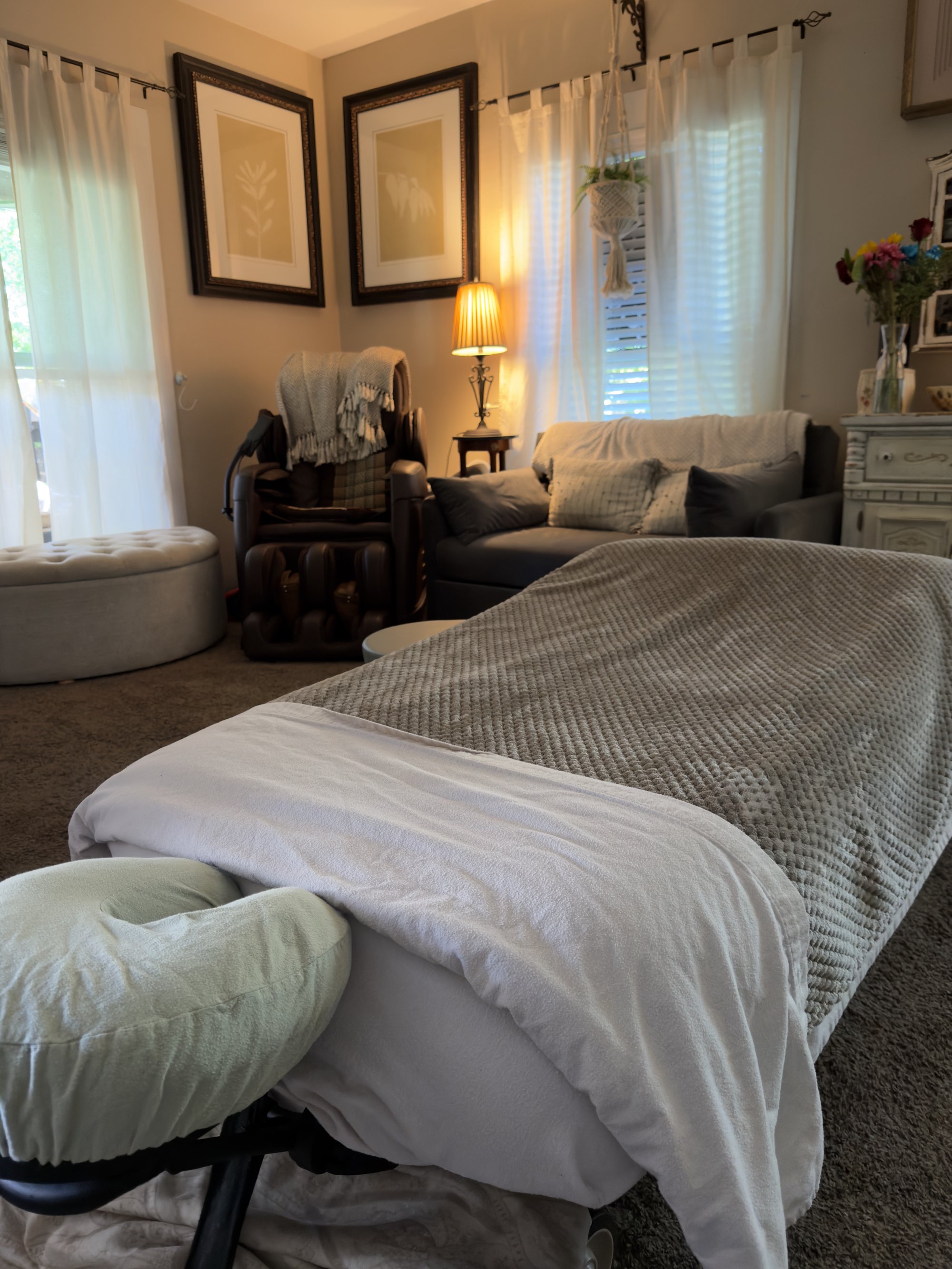 Close-up of the massage table head — knit-textured throw, white face-cradle cover, deep blue privacy curtain, and a soft daylit window beyond.