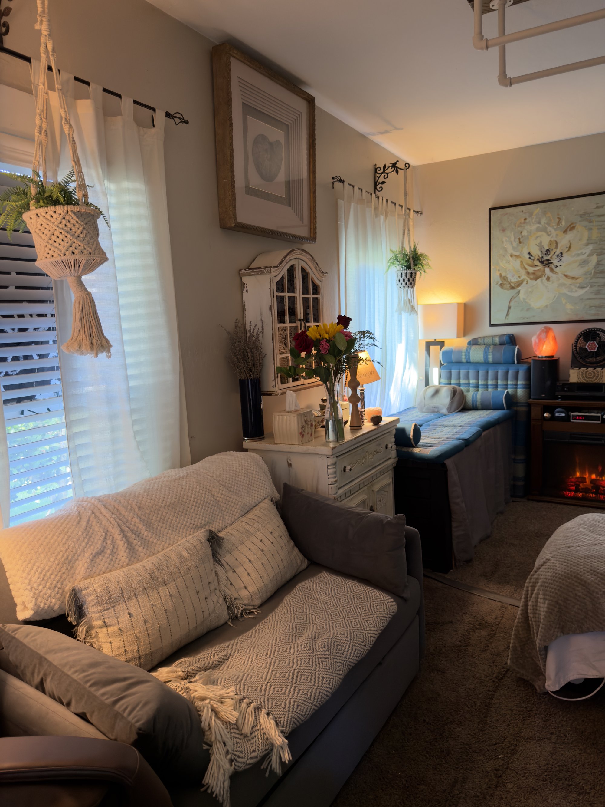 Side view of the vanity area with a grey upholstered day-bed sofa, woven throws, framed art, and a hanging macramé on the wall.