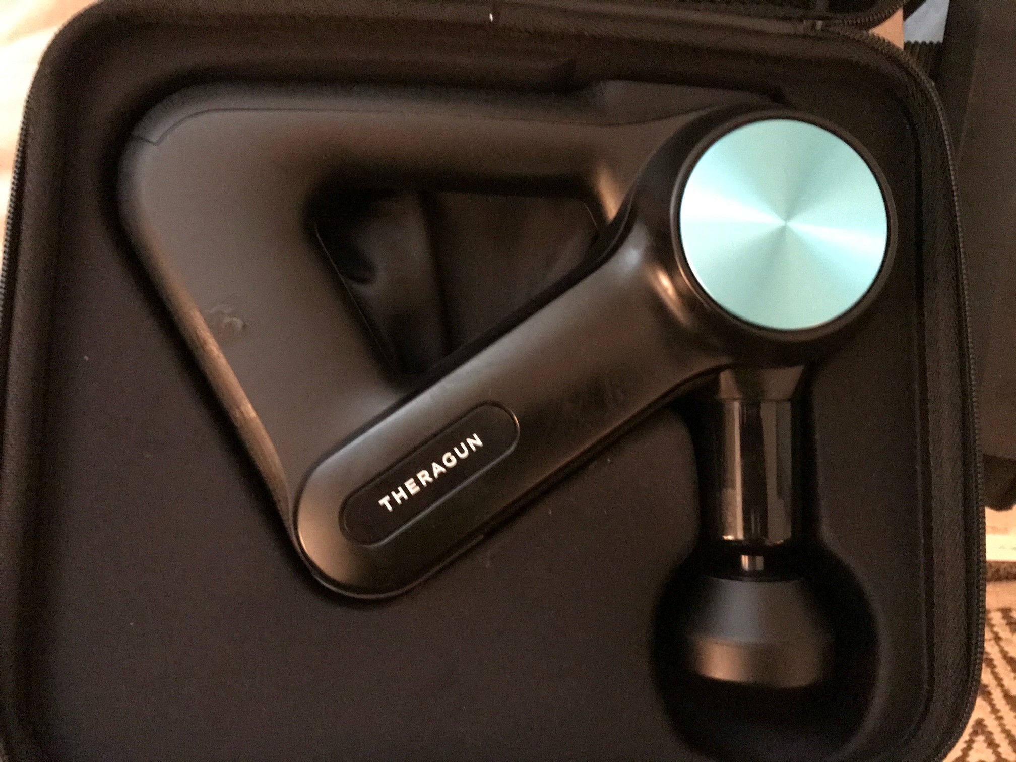 Theragun percussion-therapy device in its black zipper case.